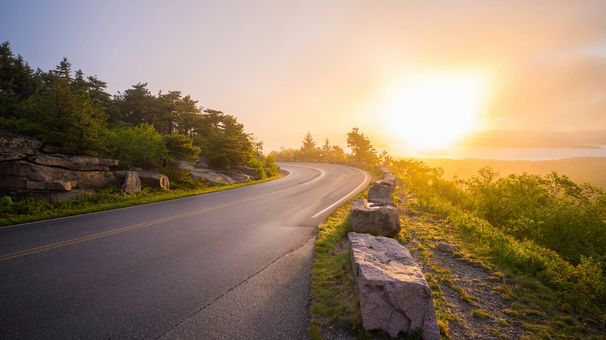An empty road curving between sunlit rock formations in late afternoon light