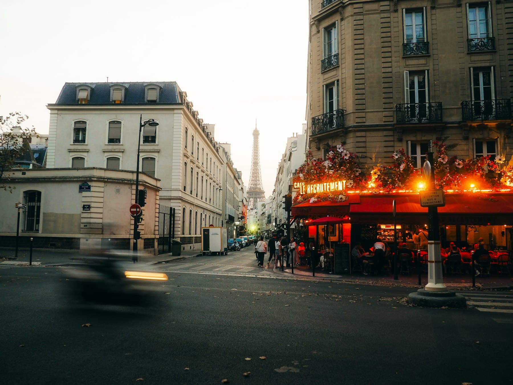 The Eiffel Tower lit at night, seen down a Parisian street past a café